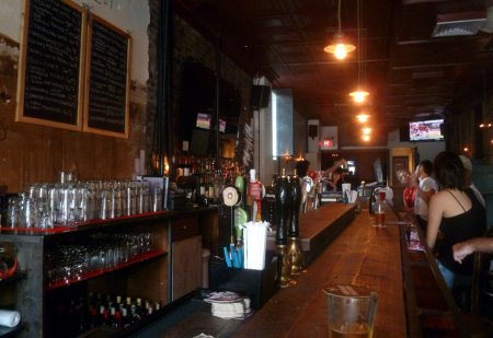 NYC beer bar interior with wooden bar counter, glassware, chalkboard menu, and patrons, circa 2012